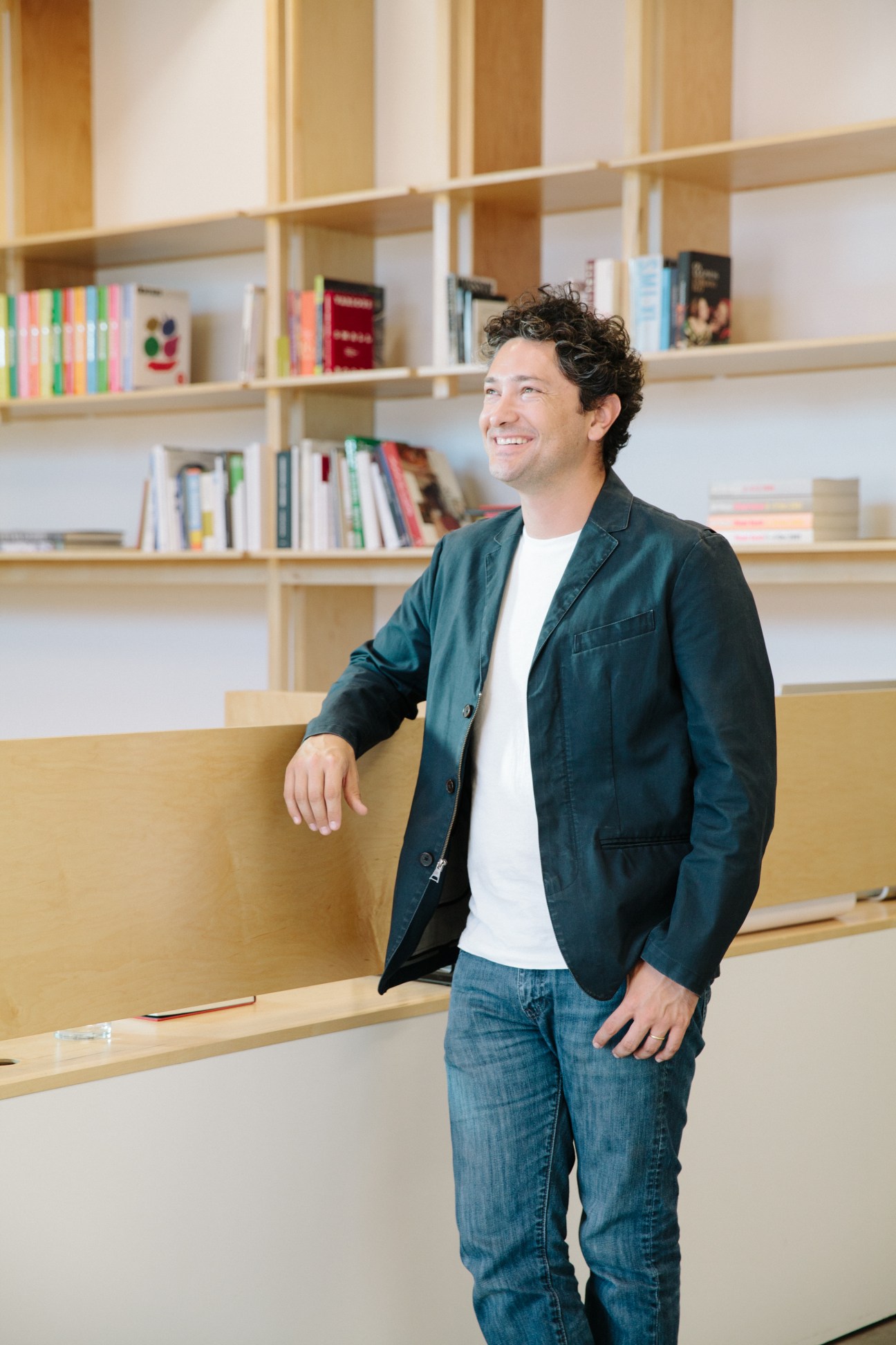 Architect Alfonso Medina stands in front of wooden shelving filled with books inside The Mistake Room gallery.