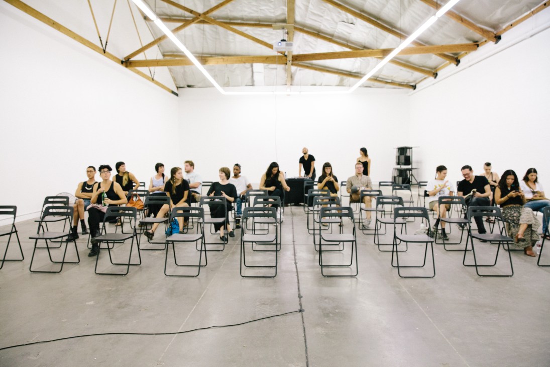 Visitors seated on black chairs in The Mistake Room's minimalist white gallery space await a screening.