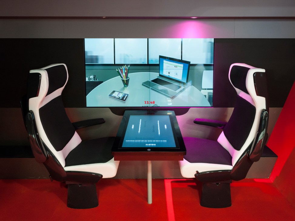 Futuristic Alstom booth display with ergonomic white and black seats facing a touch-screen table and wall-mounted screens.