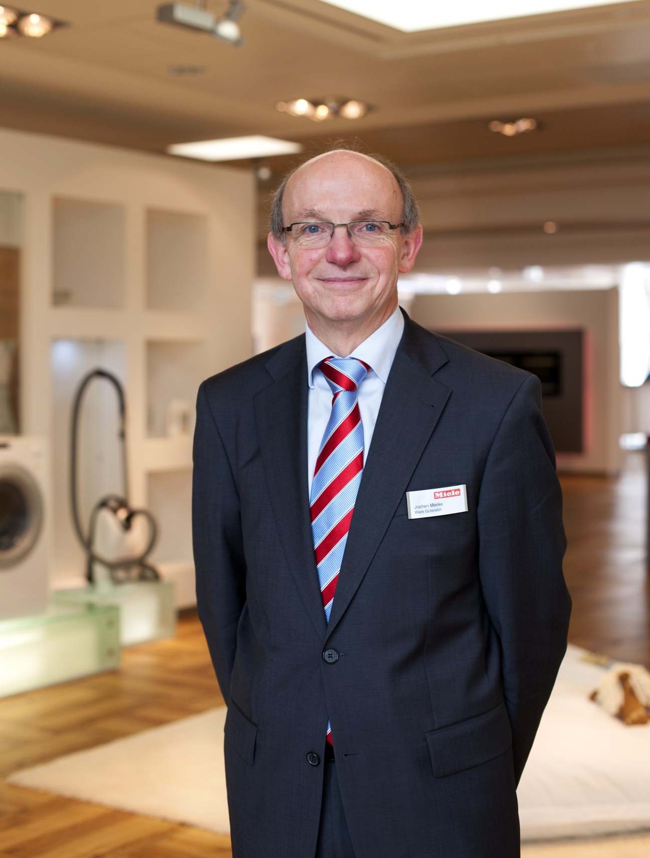 Jochen Menke, a Miele factory guide, stands in professional business attire in a showroom displaying appliances.