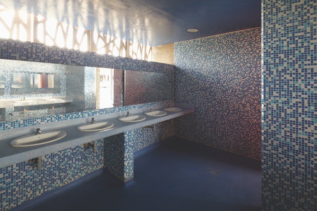 School bathroom with blue and white mosaic tile walls and multiple white sinks along a counter.