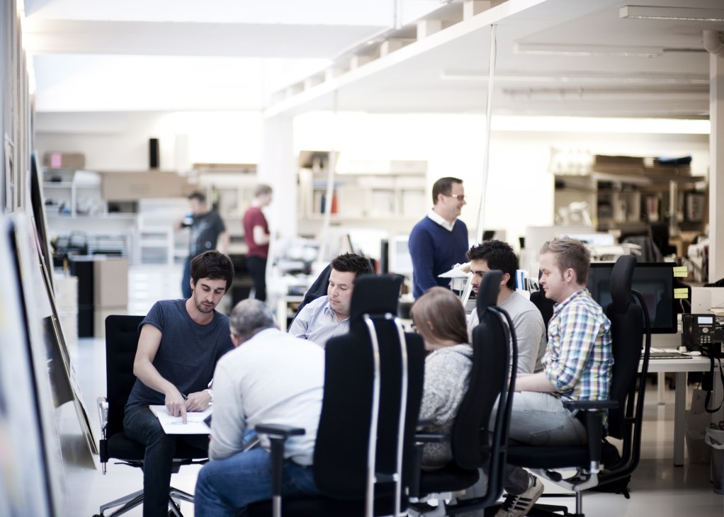 Team members collaborate around a table in a bright, modern design studio office space.