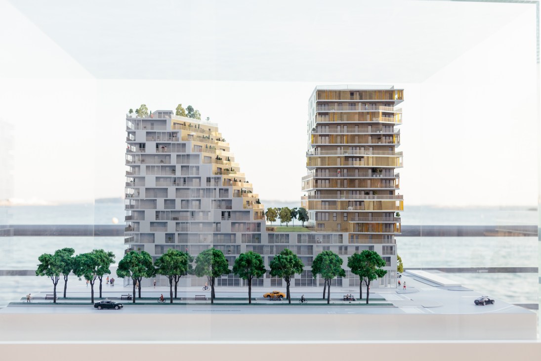 Architectural rendering of a modern residential building with multiple towers featuring gold and grey facades alongside a waterfront.