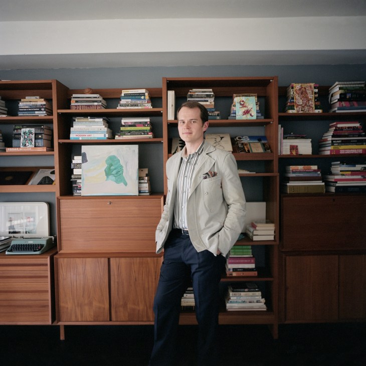 James Pike stands in front of a large wooden wall system filled with books and artwork in his Marina City studio apartment.