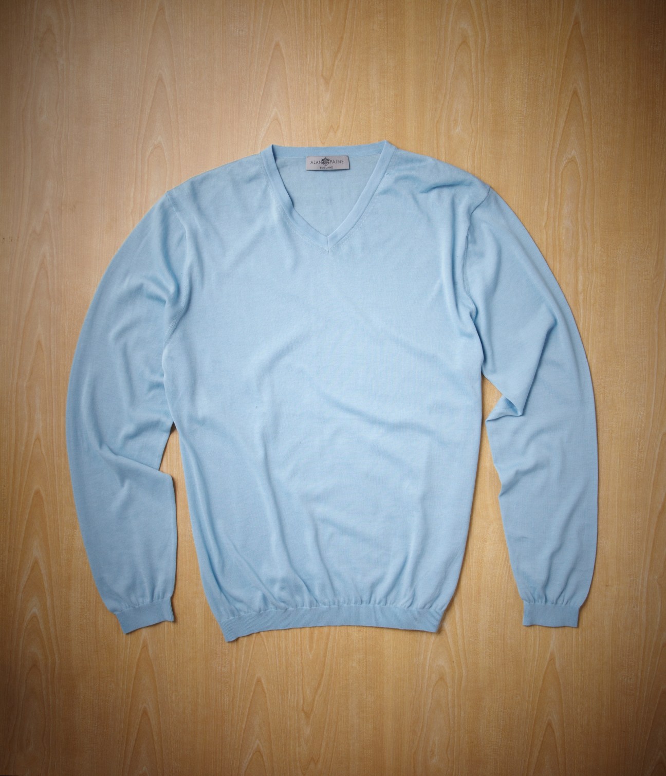 Light blue v-neck knit sweater on wooden background.
