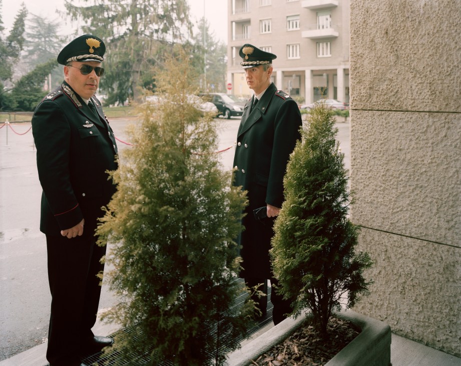 Two Italian Carabinieri officers in dark uniforms and berets stand in a courtyard.