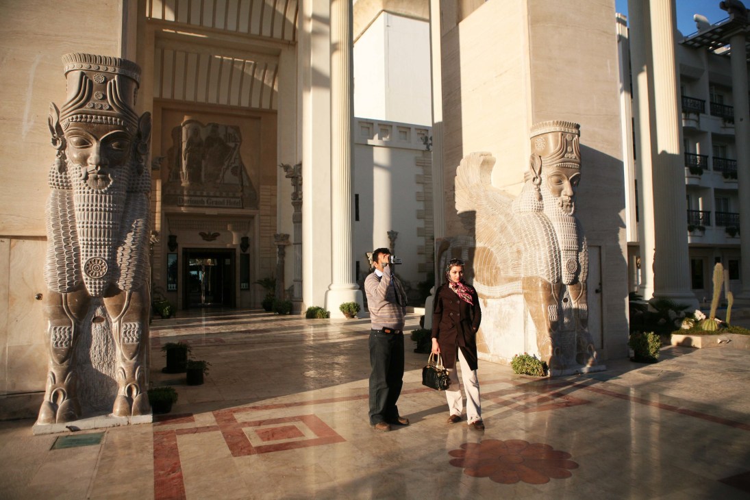 Two tourists stand in a courtyard with large Persian stone statues flanking the space at the Dariush hotel.