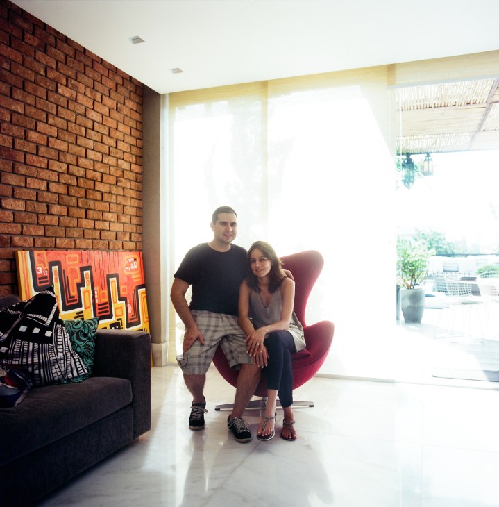 Residents Alberto and Manoela Lott sitting in a modern living room with exposed brick wall and contemporary art.