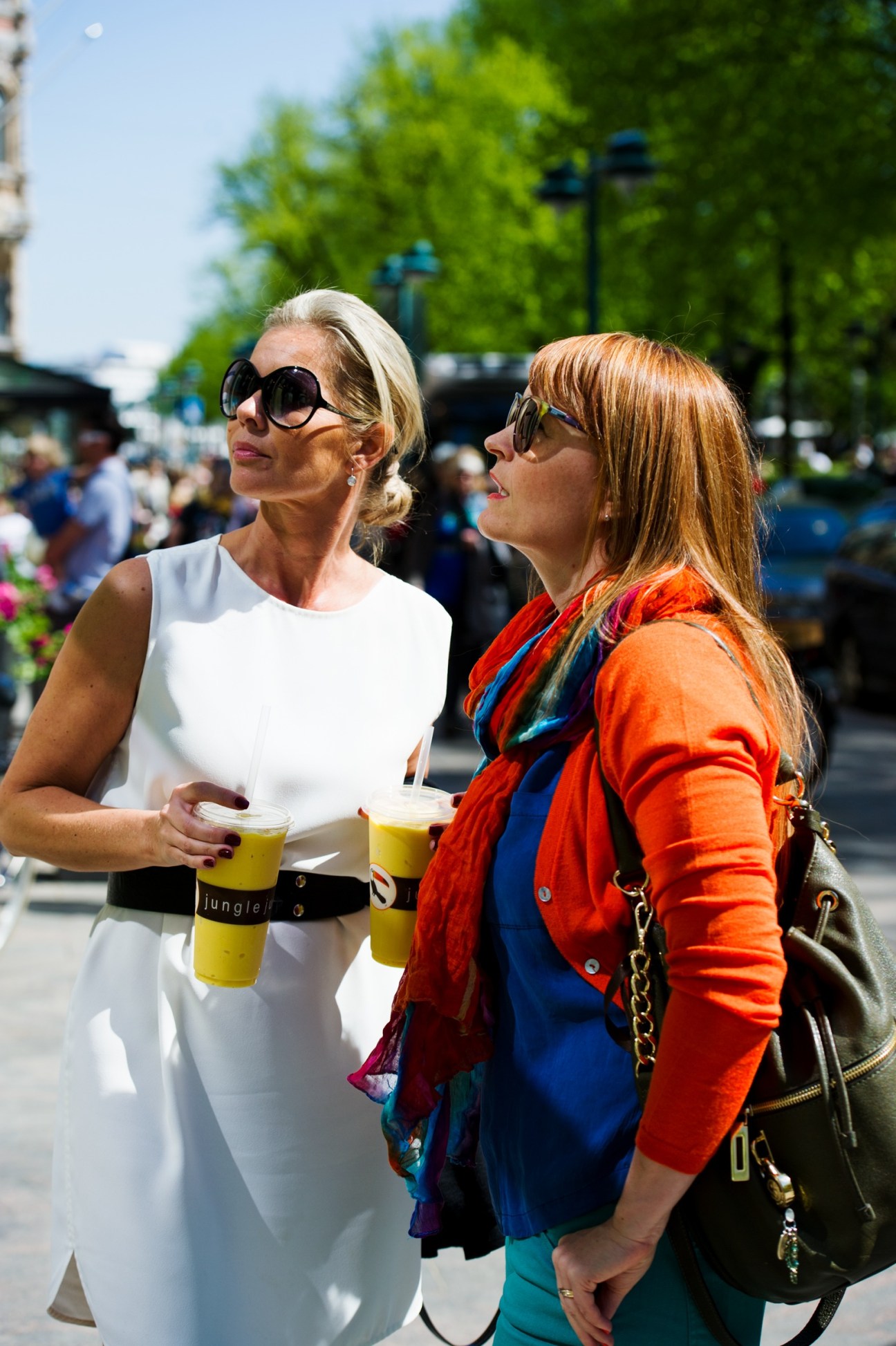 Two women enjoying drinks outdoors in a city park on a sunny day.