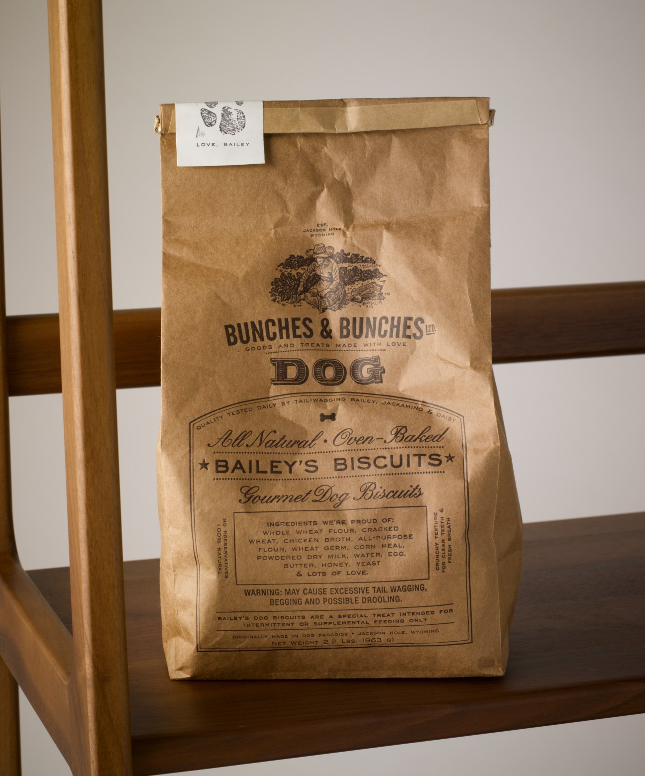 Bunches & Bunches Bailey's Dog Biscuits package in brown kraft paper on wooden shelf.