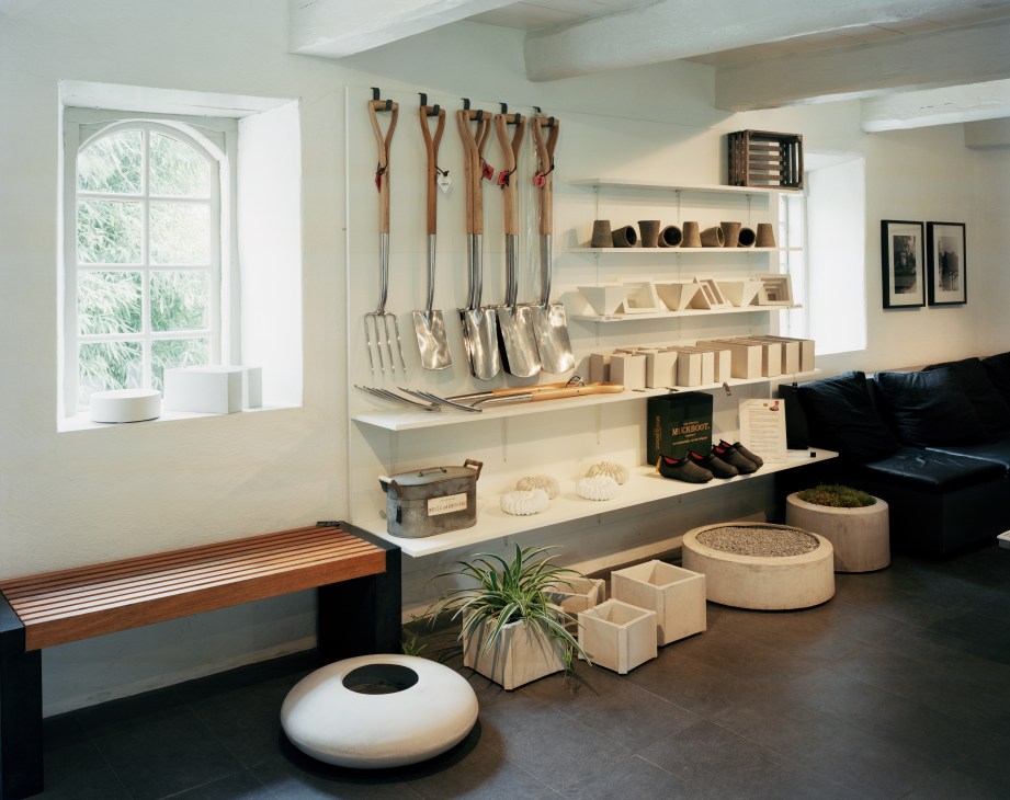 Interior of Skulpturfabriken shop displaying Stina Lindholm's concrete designs and gardening tools on white shelves.