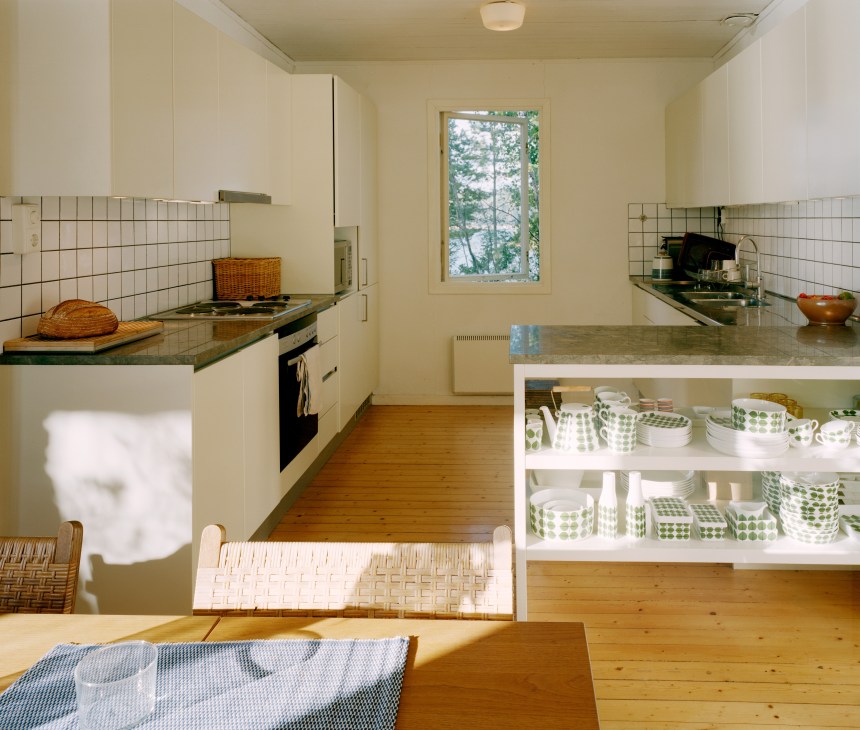 Open-plan kitchen with white cabinetry, white tile backsplash, and open shelving displaying green and white patterned Gustavsberg crockery.