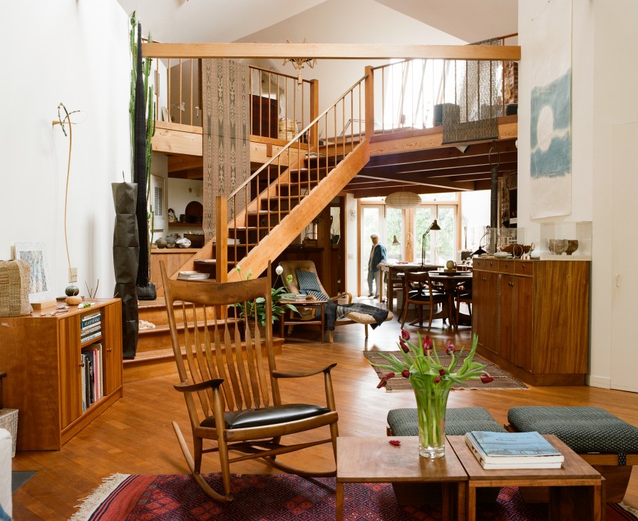 Open-plan interior of Kay Sekimachi's home showing wooden furniture, diagonal ceiling beams, and a mezzanine level.
