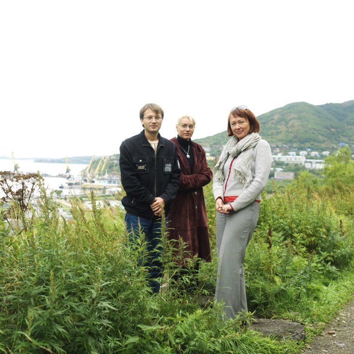 Tatyana Mikhailova and two colleagues stand in overgrown vegetation overlooking Petropavlovsk and Avacha Bay.