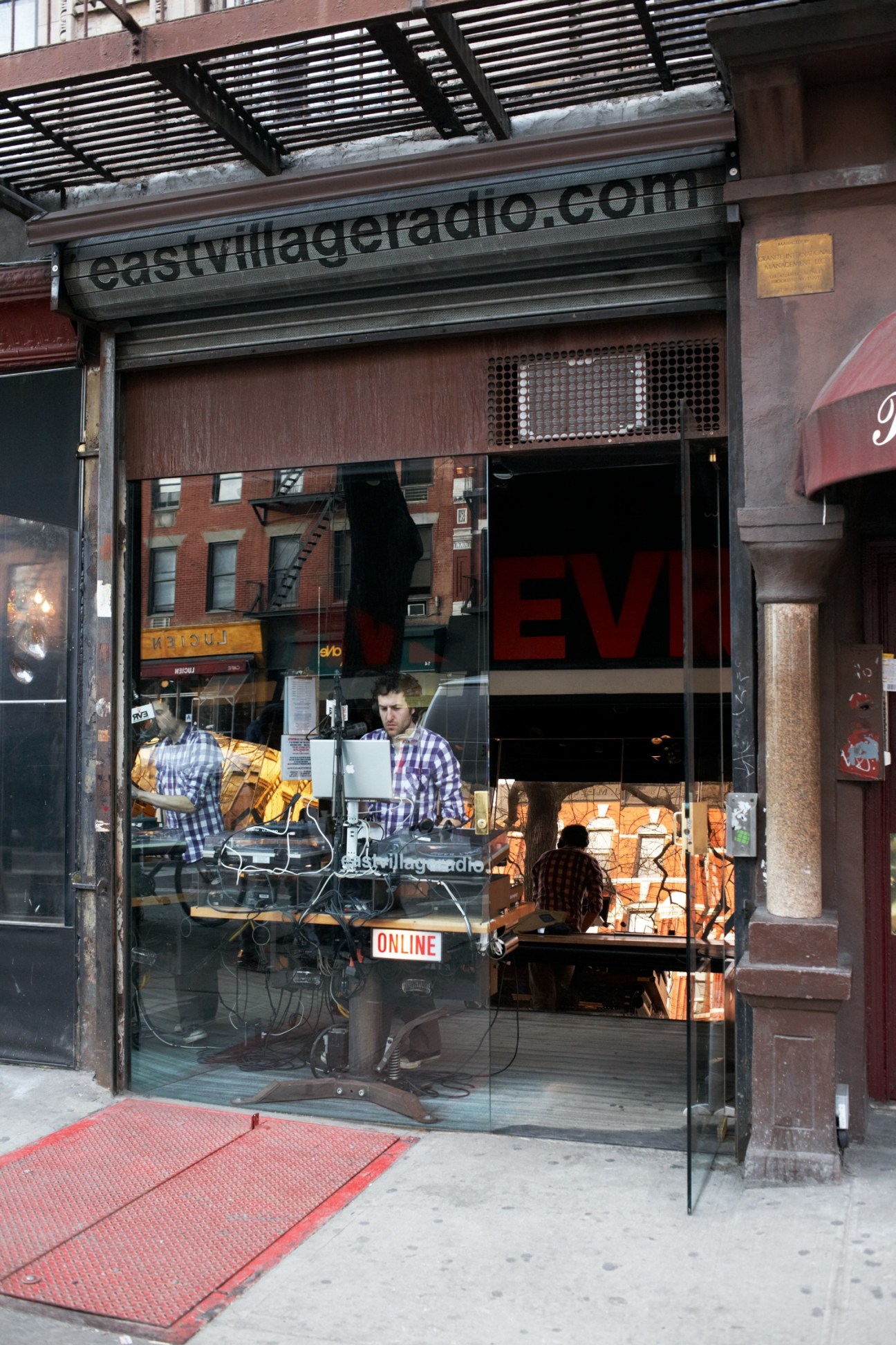 East Village Radio's glass-fronted studio on First Avenue in New York with DJs visible at equipment inside.