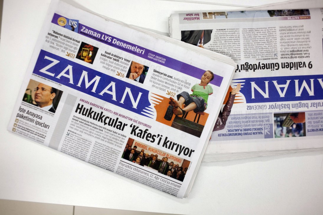 Turkish newspapers including Zaman displayed on a white surface, showing colorful front pages with Turkish text and imagery.