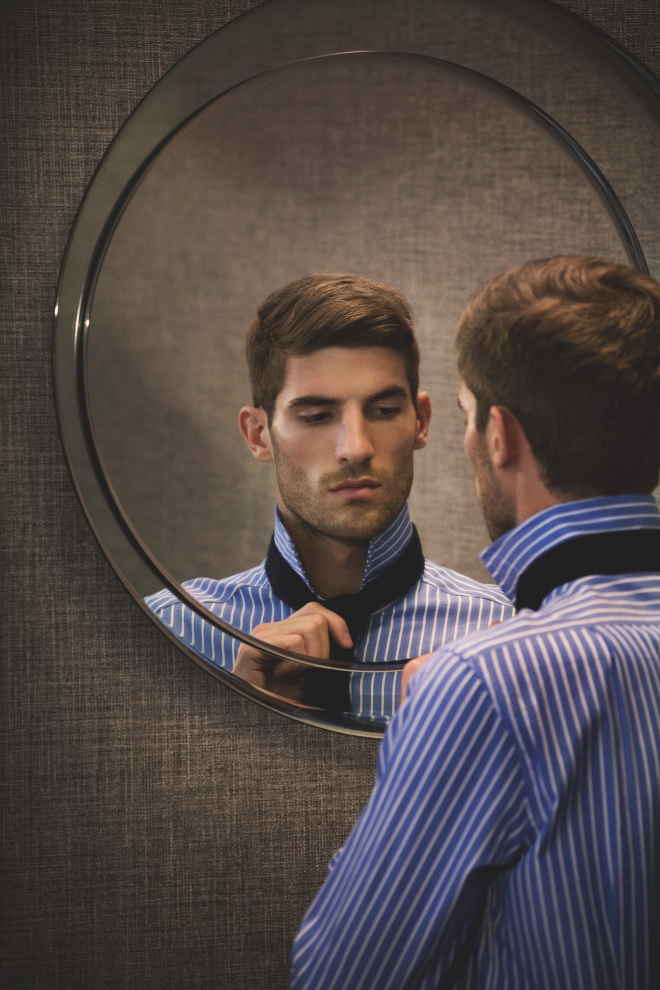 Man in blue striped shirt by E.Tautz and Hackett tie viewing his reflection in a circular mirror.
