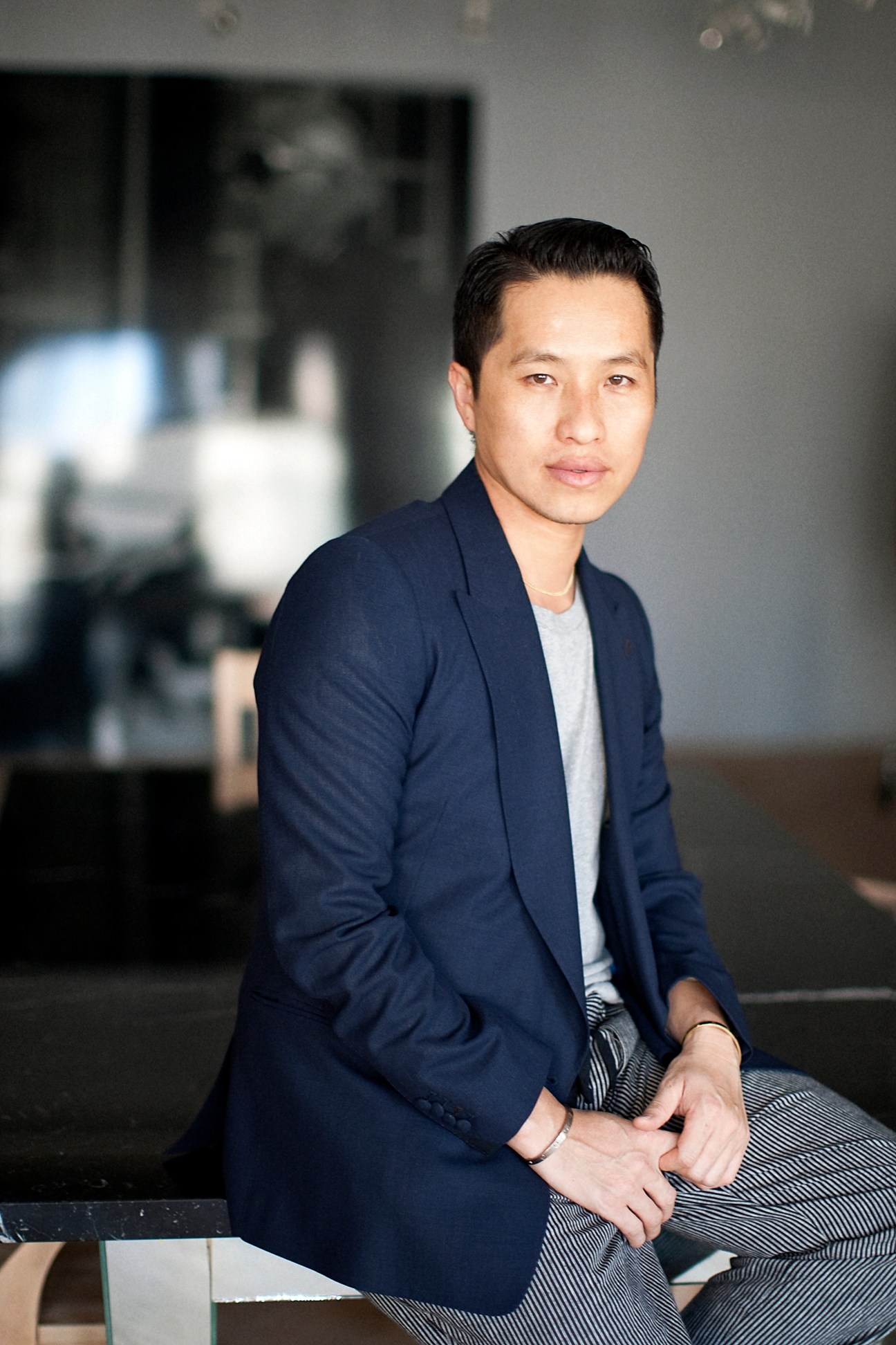 Man wearing navy blazer and striped trousers sitting indoors.
