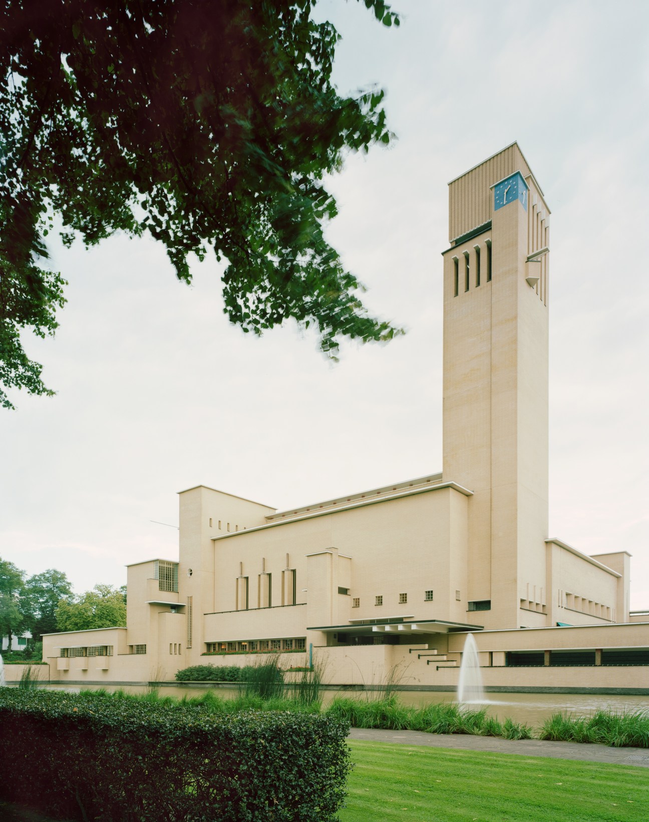 Dudok-designed town hall with tall clock tower, cream-colored modernist architecture and manicured grounds.