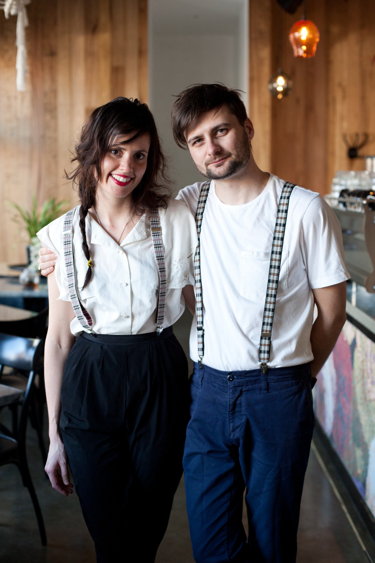 Two young restaurant owners stand together in The Brix dining room with warm lighting and exposed brick walls.