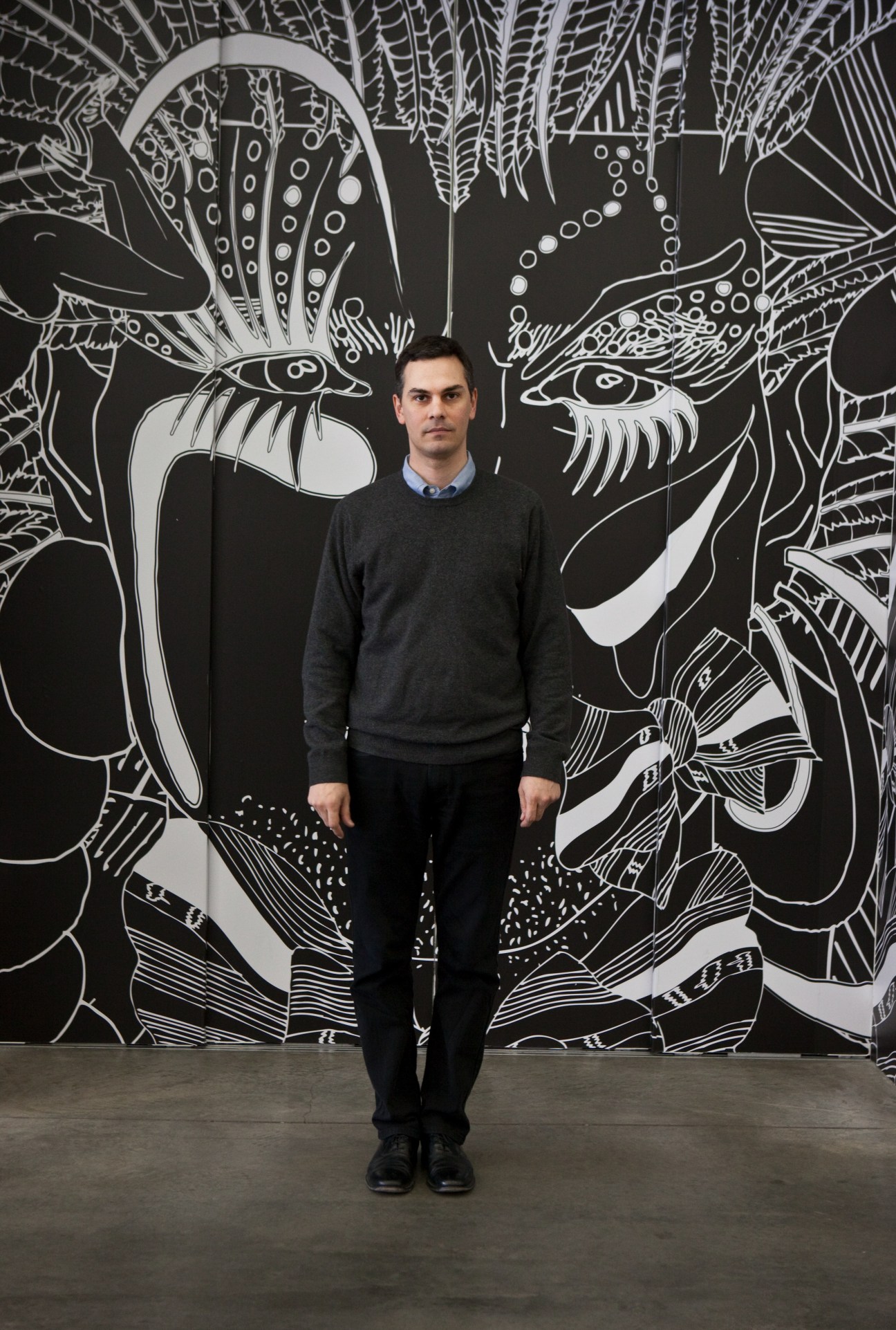 Massimiliano Gioni, director of special exhibitions at the New Museum, stands before a large black and white abstract artwork.