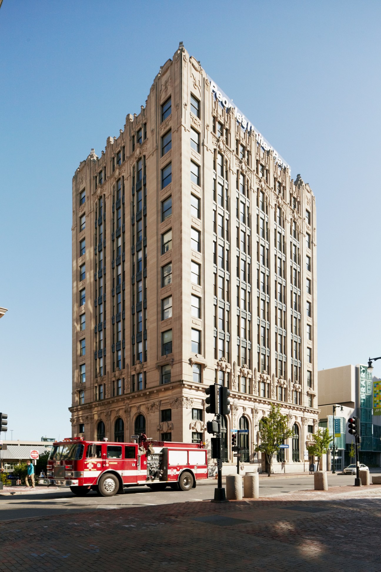 Red fire truck parked in front of a historic tan brick building with ornate architectural details under clear blue sky.