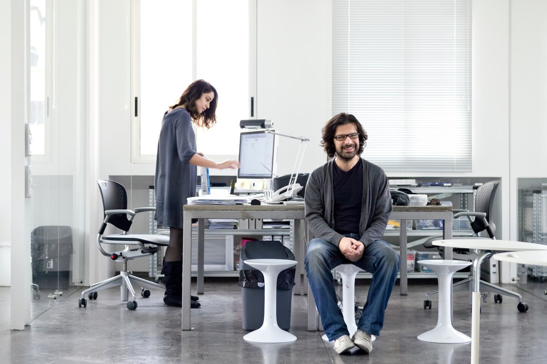 Two people in a modern office space with floor-to-ceiling windows and minimalist furniture.