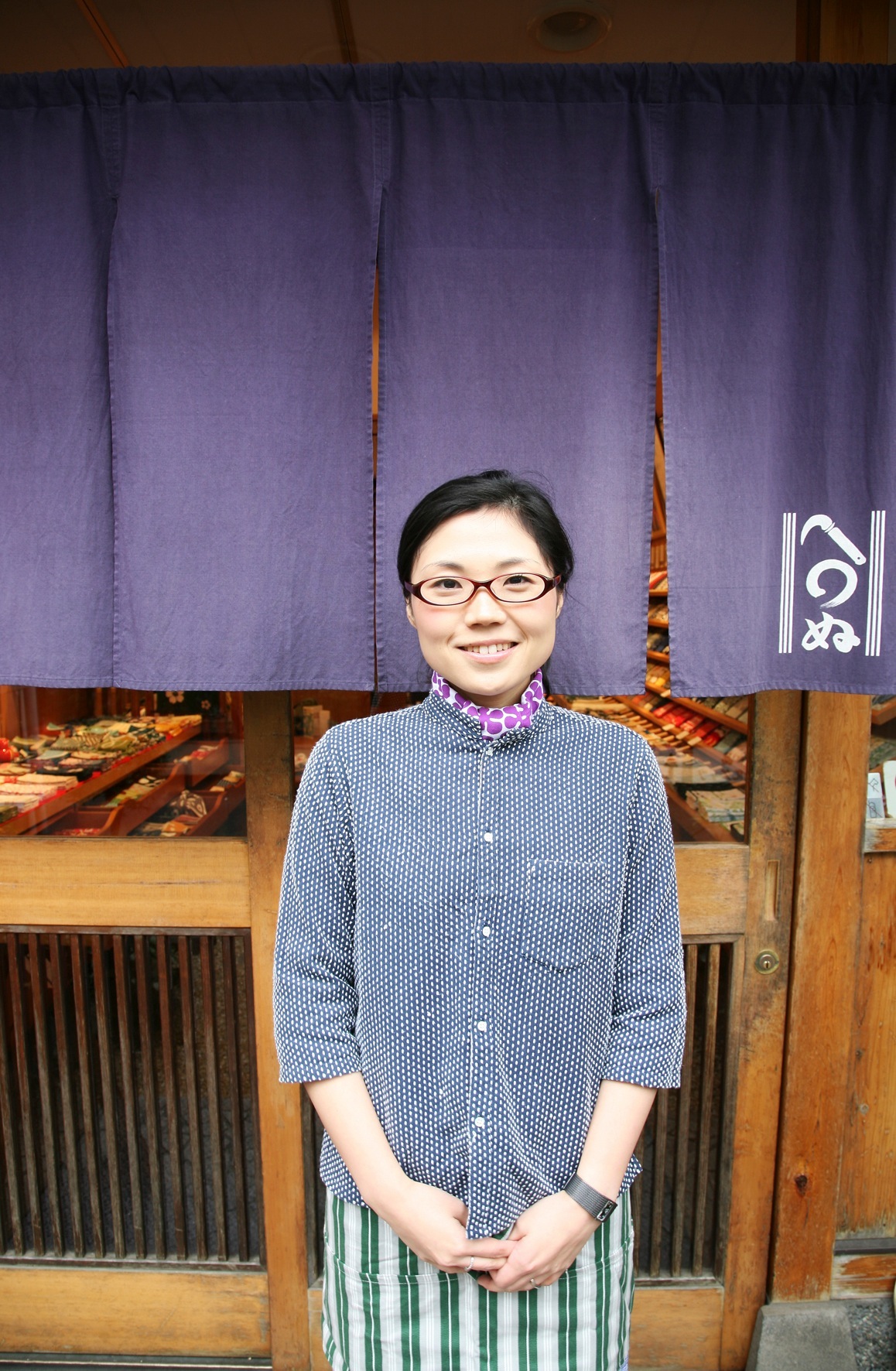 Woman smiling at Kamawanu shop entrance with purple noren curtain and wooden storefront.