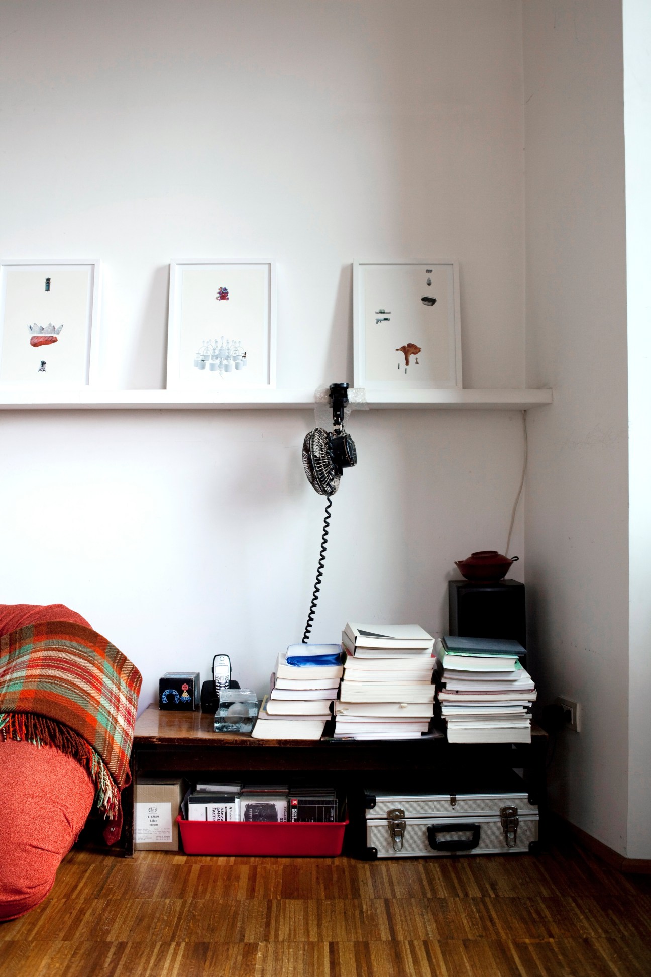 Interior corner with framed artwork, stacked books, vintage telephone, and orange patterned textile in Elly Nagaoka's house.
