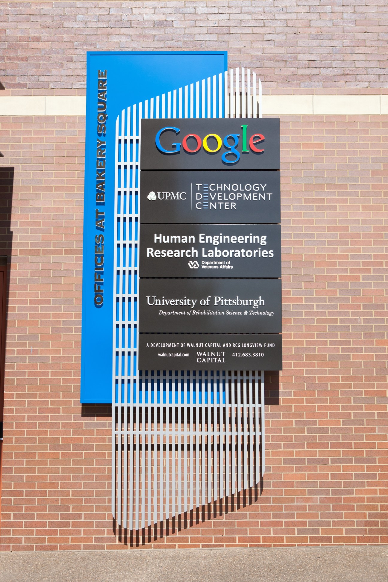 Bakery Square building signage displaying Google, UPMC Technology Development Center, Human Engineering Research Laboratories, and University of Pittsburgh logos on brick facade.