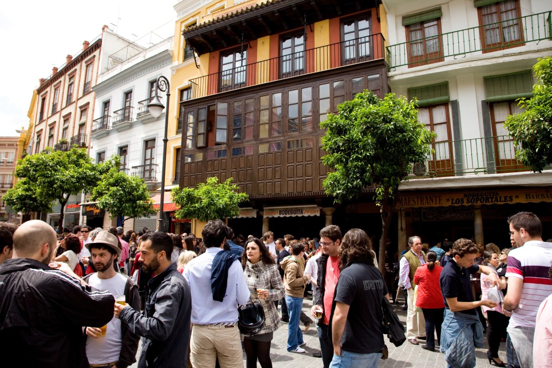 Crowded plaza in Seville with colorful historic buildings and outdoor café seating.