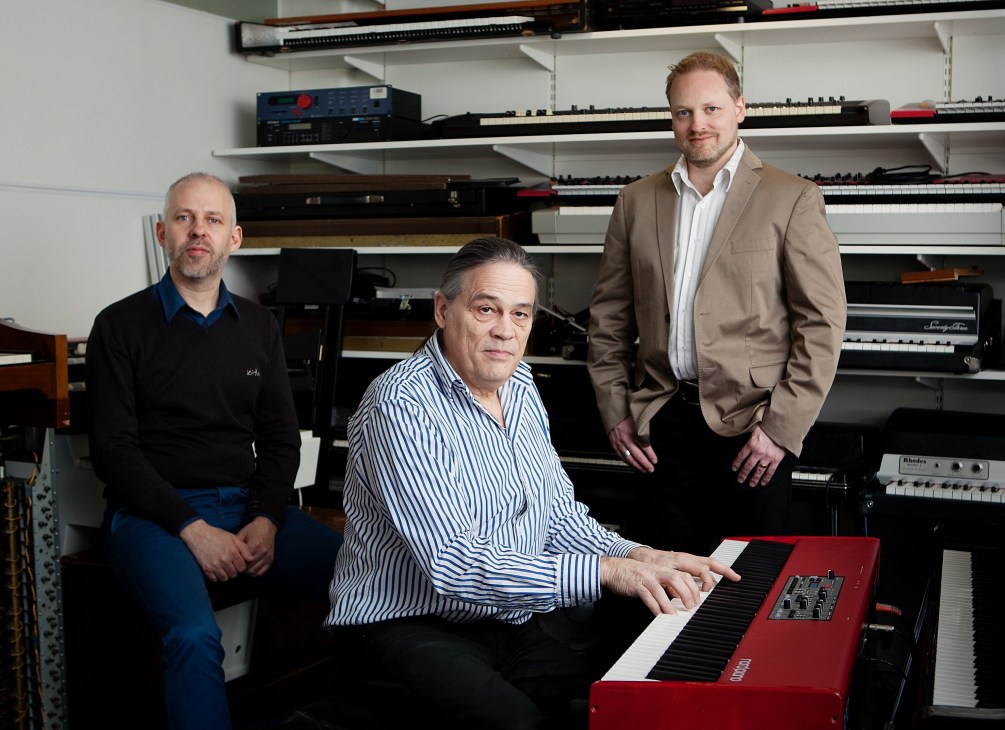 CEO Hans Nordelius and head of software Magnus Kjellander pose at a red Nord keyboard in Stockholm factory with instruments on shelves behind them.