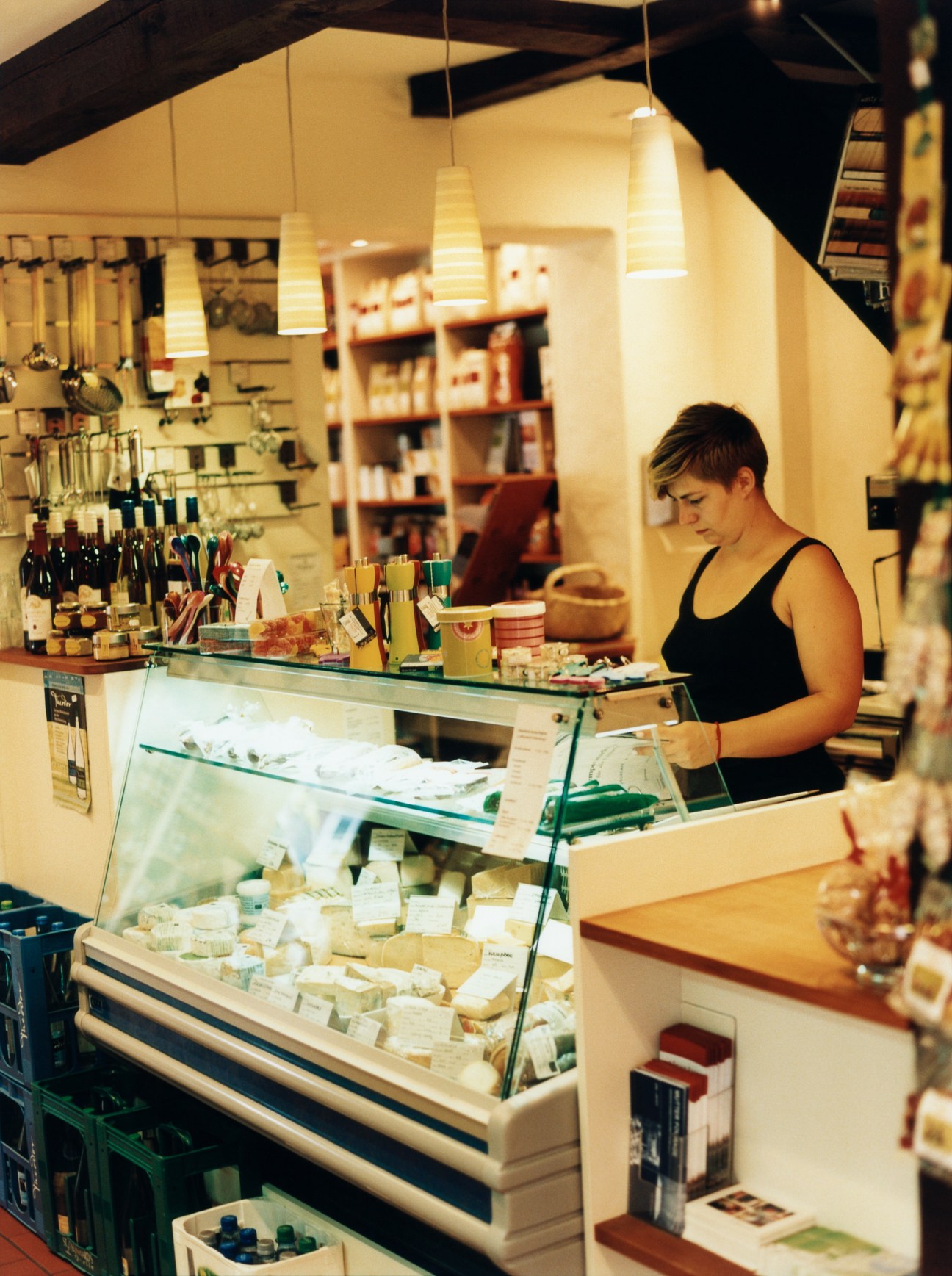 Staff member at the counter of Mutter Fourage deli displaying cheese and cakes in a glass display case.