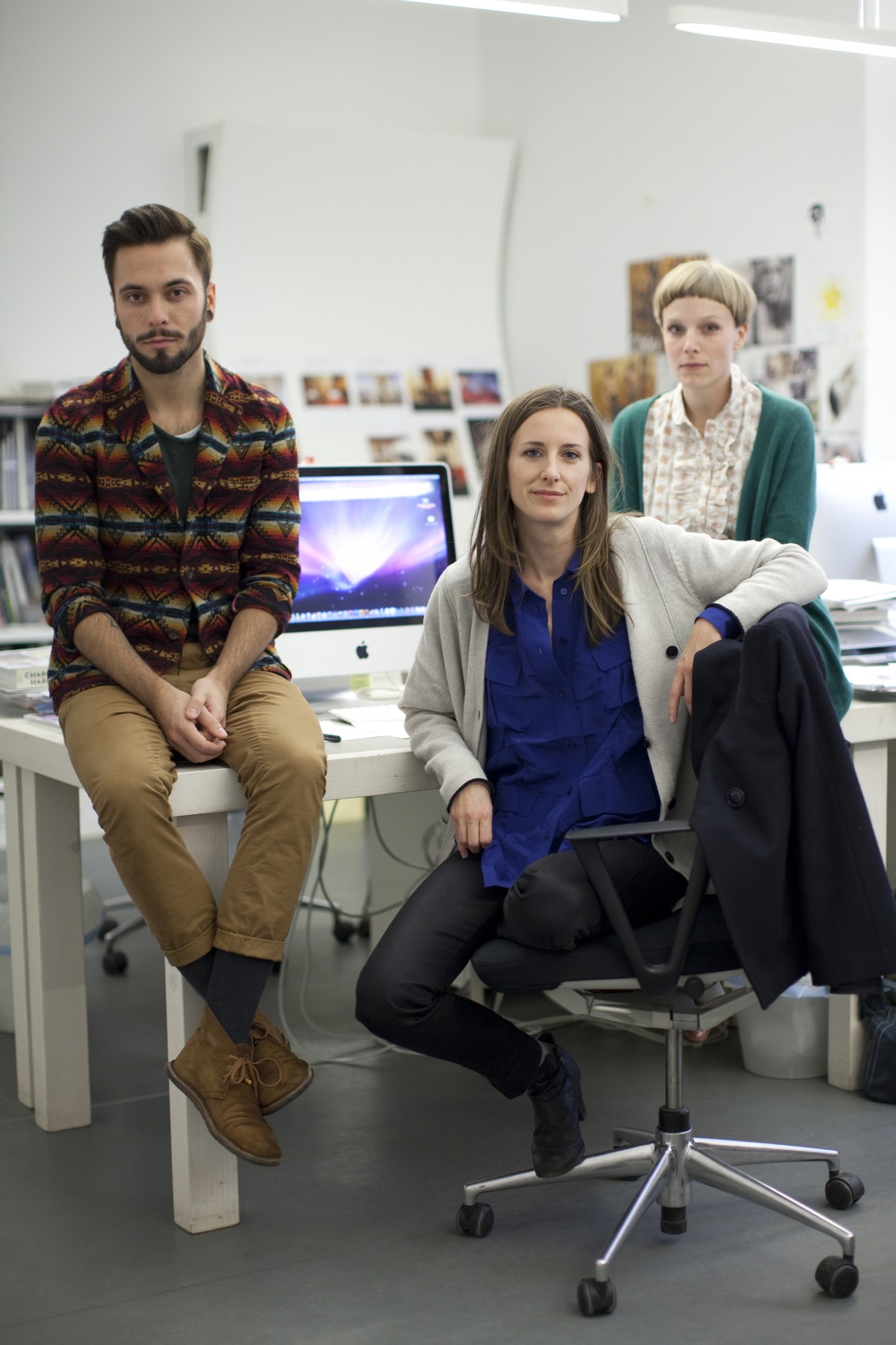 Four staff members posed in a modern office space with computers and artwork on walls.