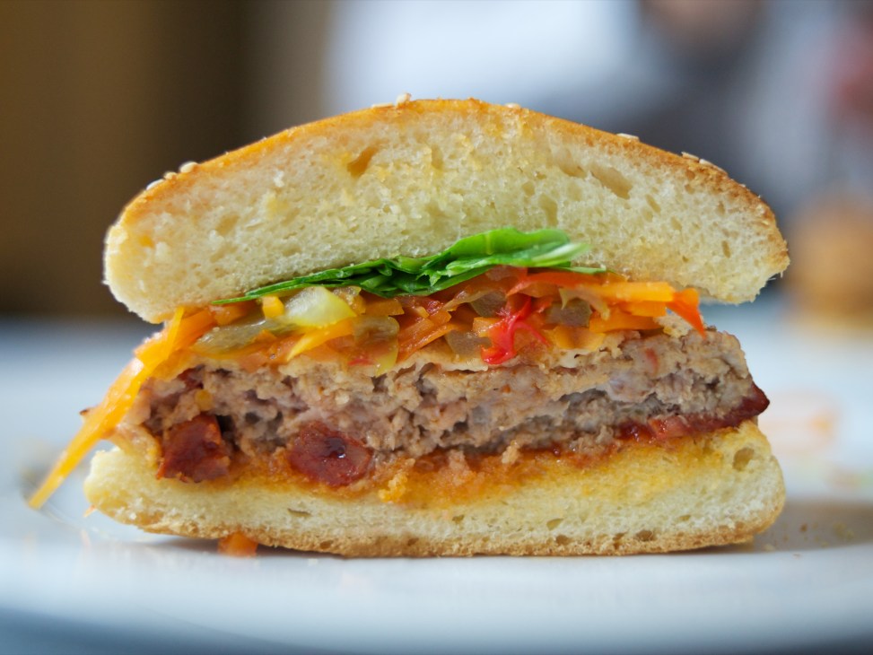A gourmet burger with melted cheese, sautéed vegetables, and fresh greens on a brioche bun.