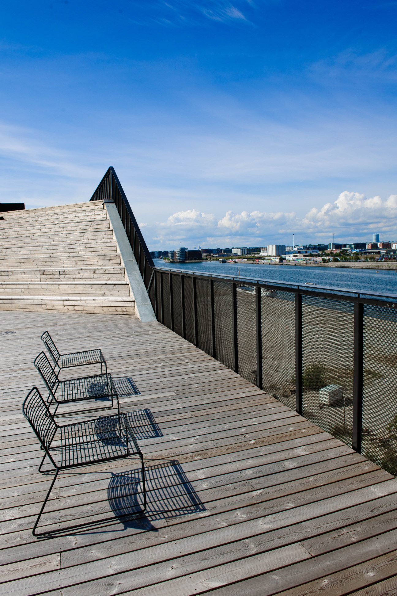Modern waterfront deck at Stay Hotel Copenhagen with metal chairs overlooking harbor and city skyline.