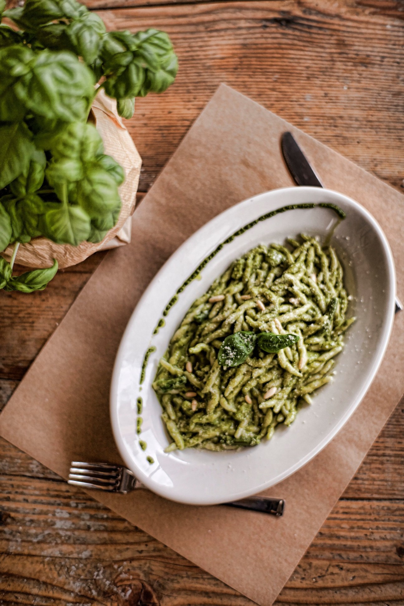 Pesto pasta dish served in a white bowl with fresh basil leaves and a fork on brown paper.