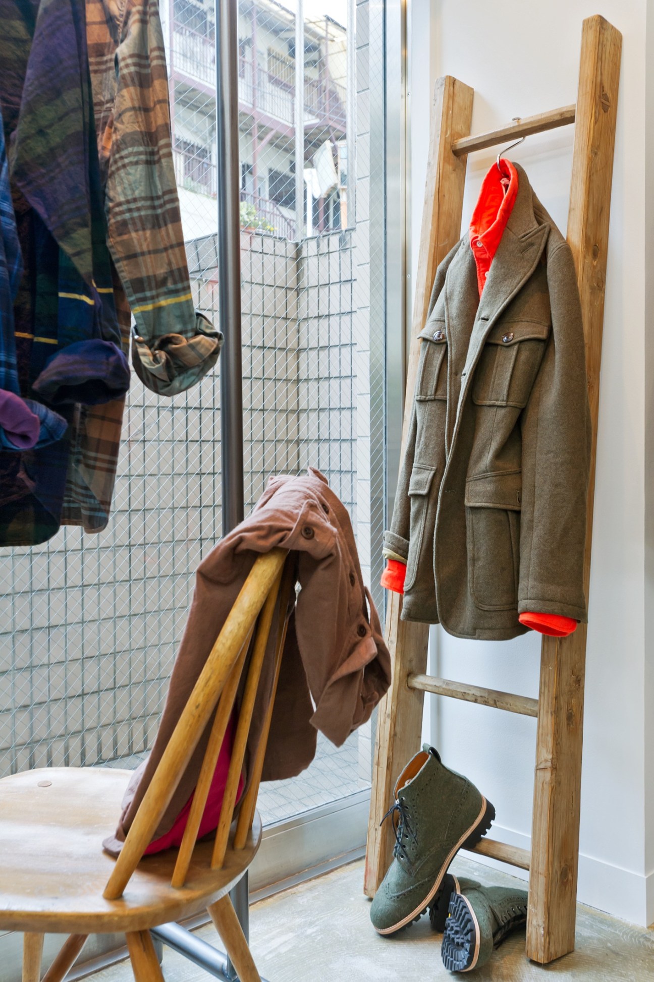 Ts(s) store display with olive jacket with red lining on wooden ladder and green boots below.
