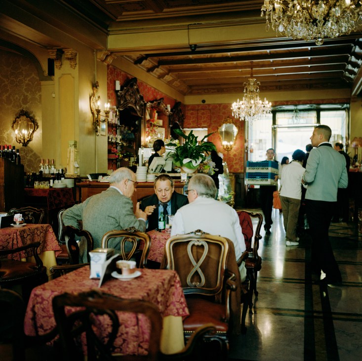 Elegant café interior with patrons seated at tables, crystal chandeliers, and ornate décor at Café Torino.