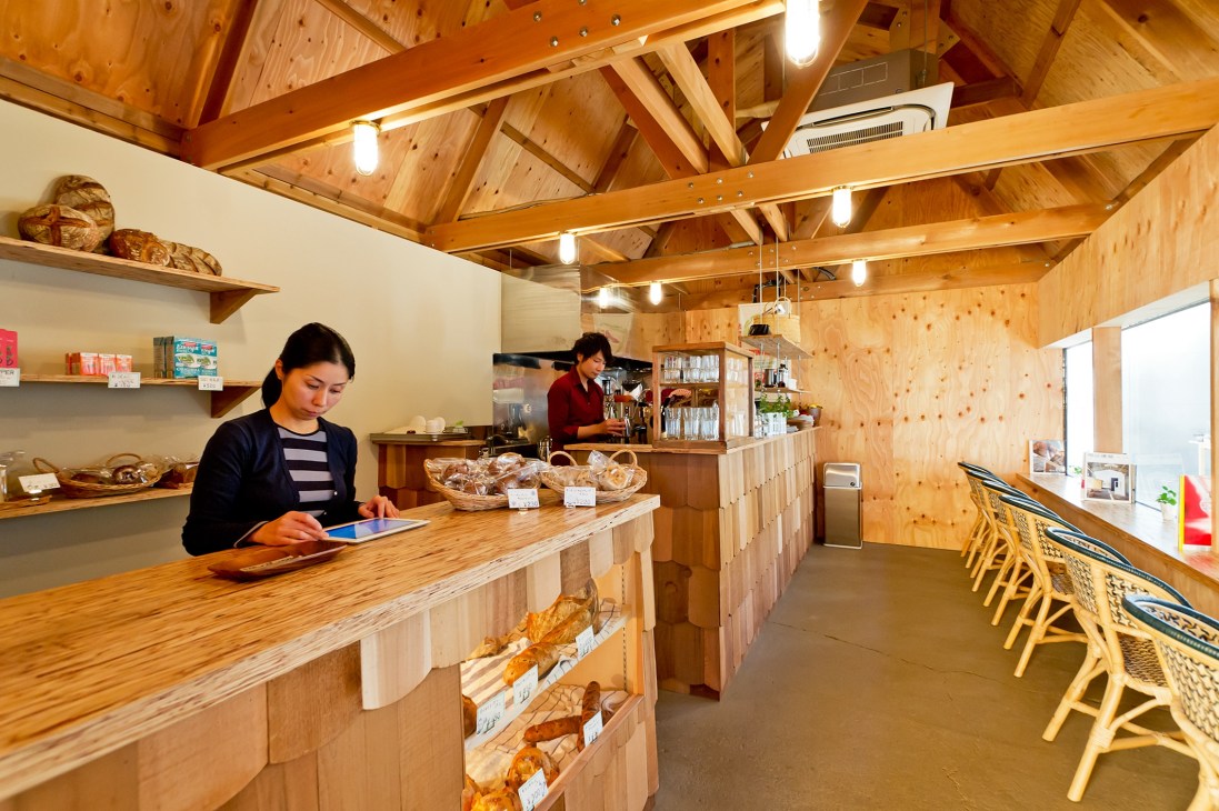 Interior of a wooden bakery and café at Newland with staff, display cases of baked goods, and wooden seating.