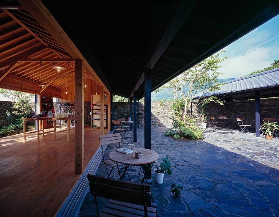 Modern residential architecture with wooden deck, stone patio, and covered outdoor living spaces overlooking mountains.