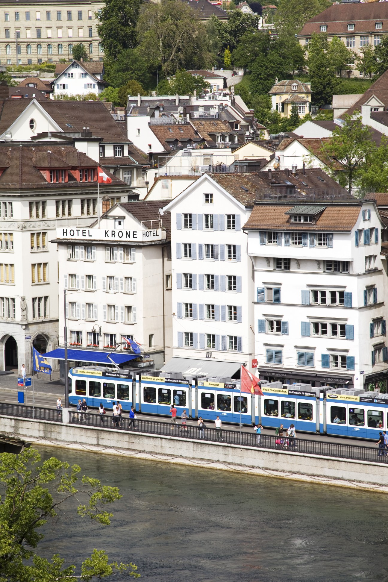 A blue and white tram travels along the Limmat River past traditional Swiss buildings in Zurich.