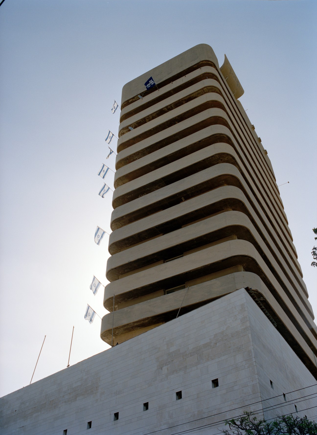 Curved modernist apartment tower with horizontal balconies and Israeli flags on King George Street in Tel Aviv.