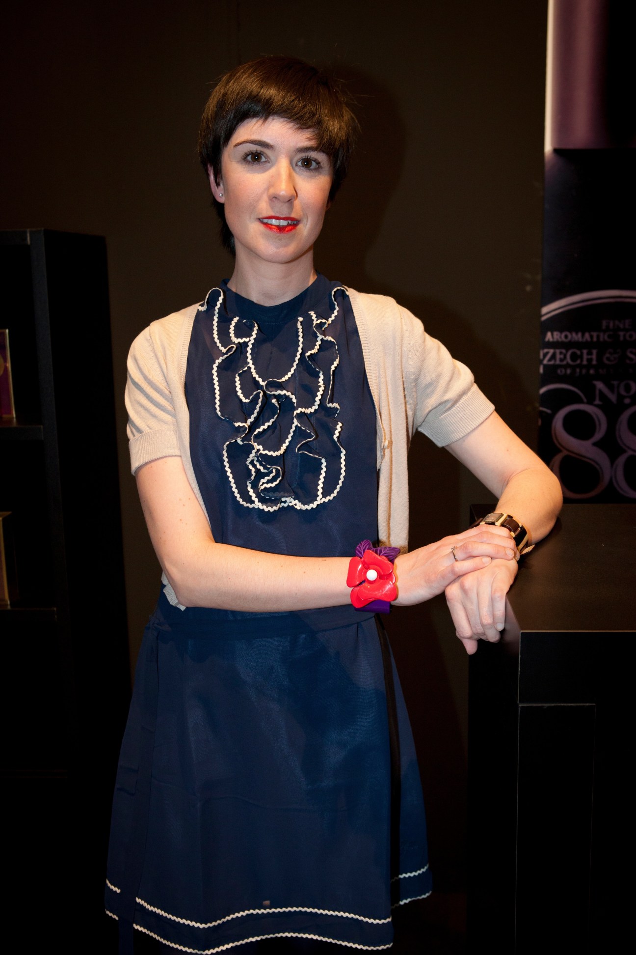 Eva Chartón, director of Perfumería Urbieta perfume shop in San Sebastián, Spain, wearing a navy dress with decorative embroidery and a red flower bracelet.
