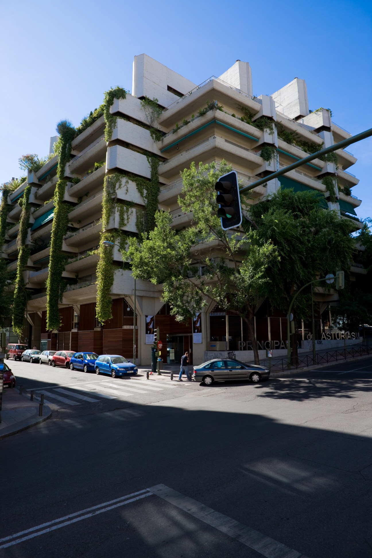 Modern multi-story apartment building with ivy-covered concrete balconies and retail space on ground floor.