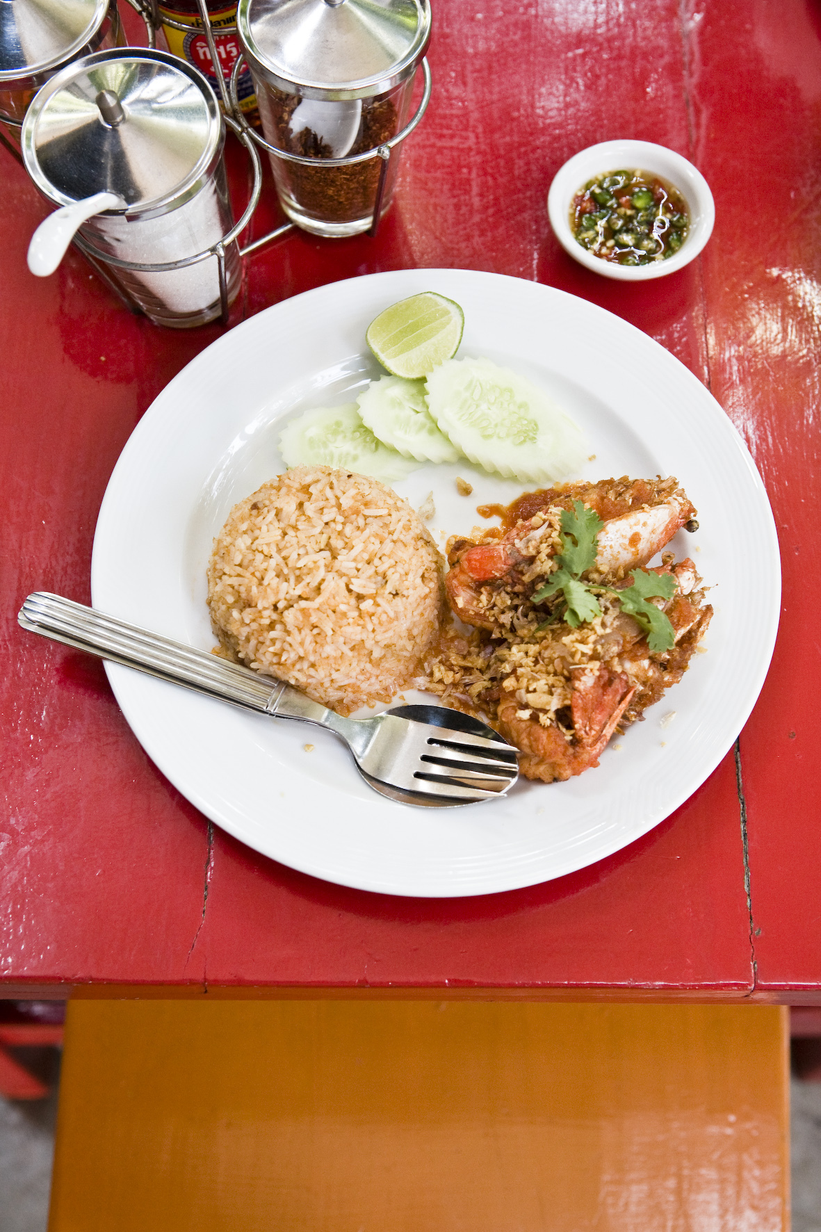Thai dish with fried meat, rice, cucumber slices and condiments on white plate at Baan Mae Yui restaurant.