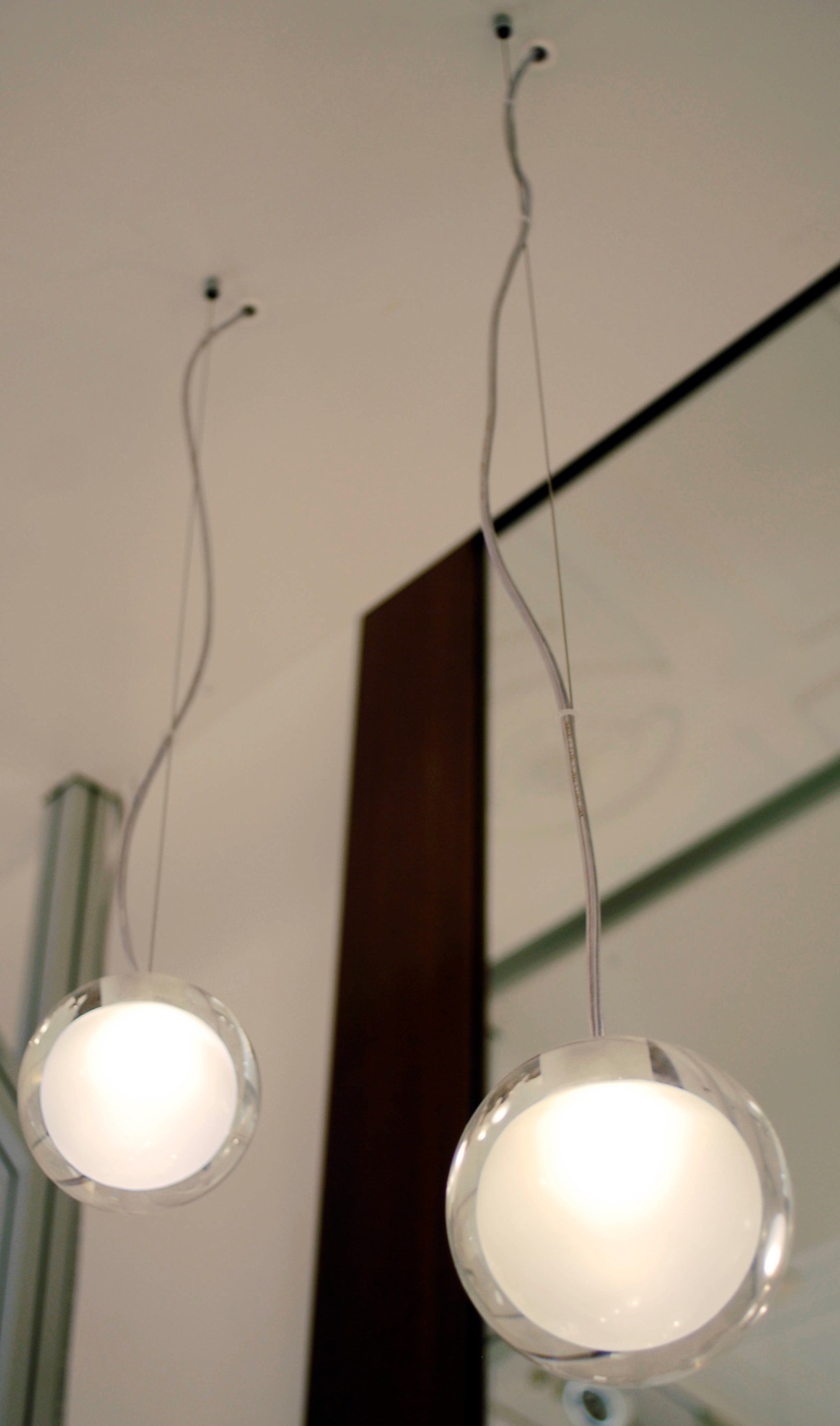 Two spherical LED pendant lights with curved wire stems hanging against a neutral wall.
