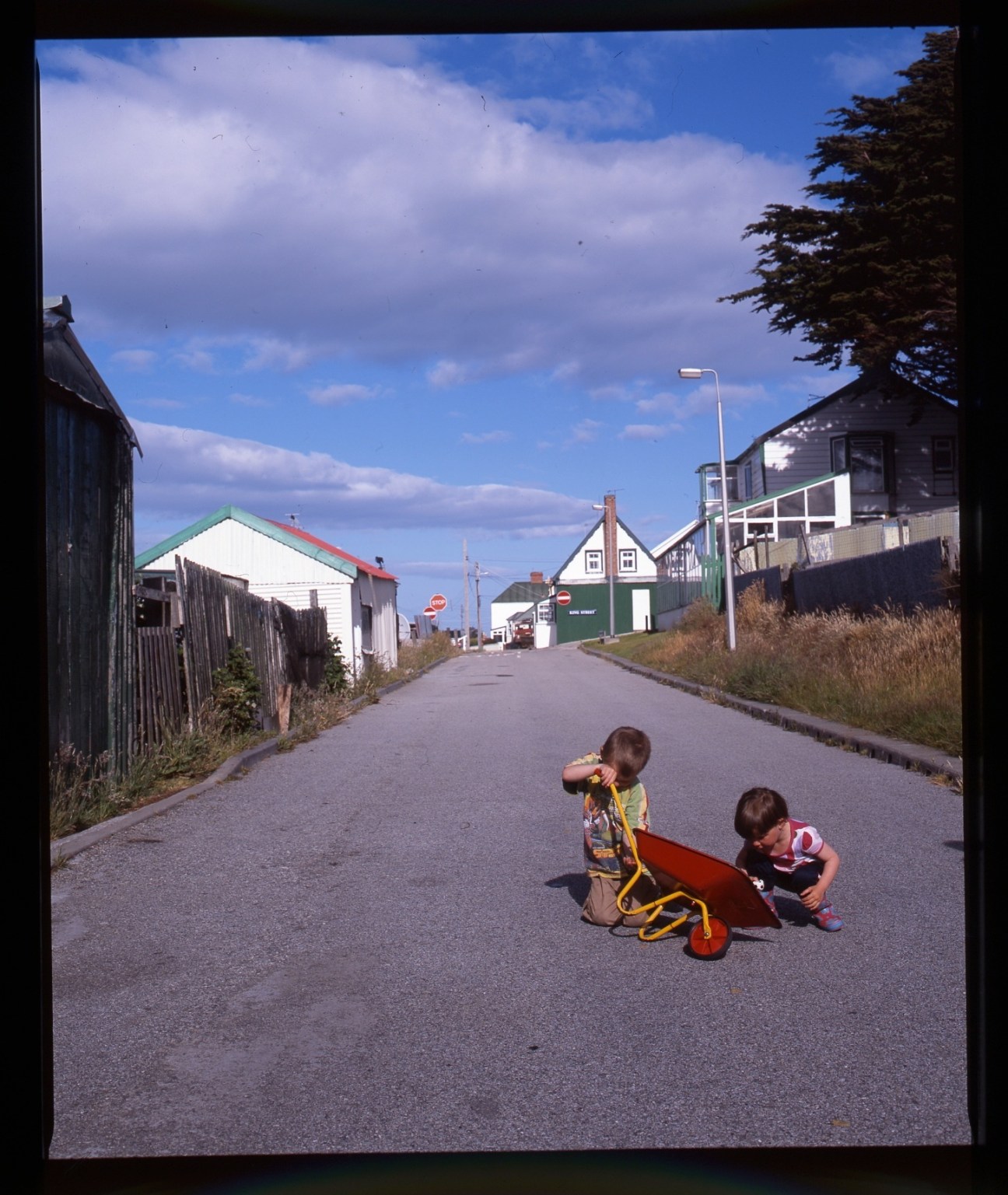 Two children playing with a red toy on a residential street lined with colorful houses in Stanley, Falkland Islands.