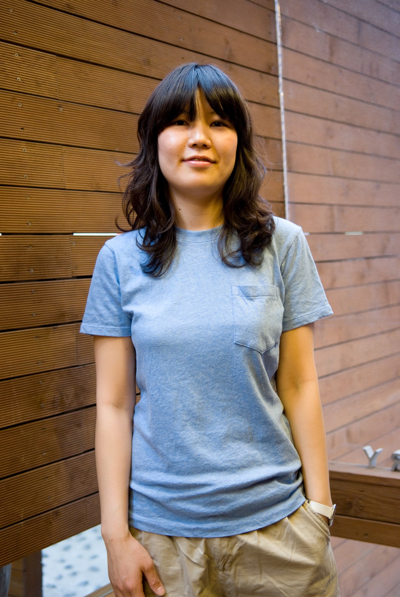 Lee Ahreum, book café manager in Seoul, standing against a wooden wall wearing a light blue t-shirt.