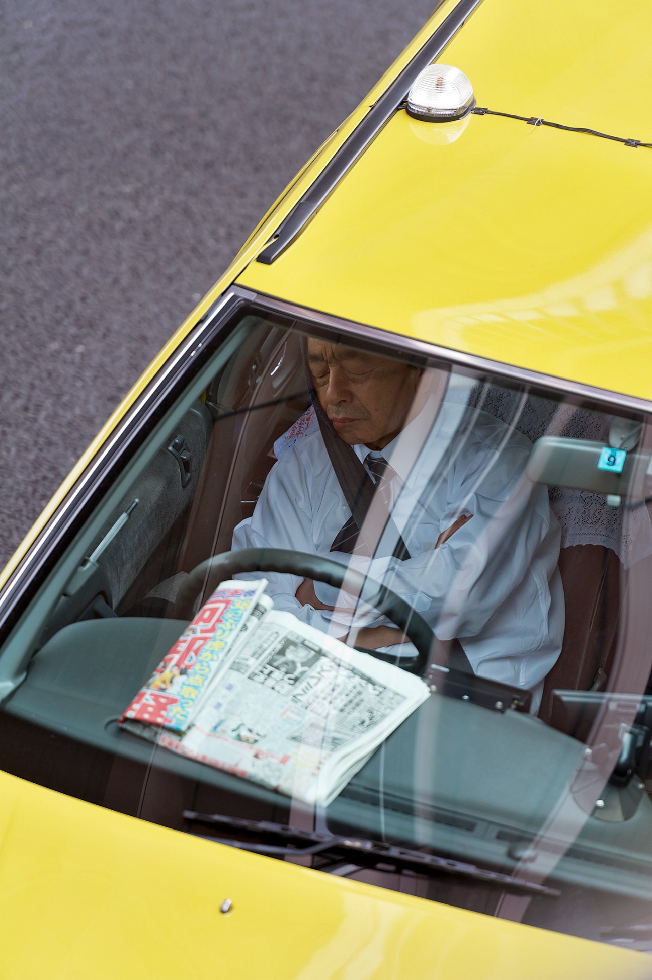 Tokyo taxi driver resting in yellow cab during shift break with newspaper on seat.